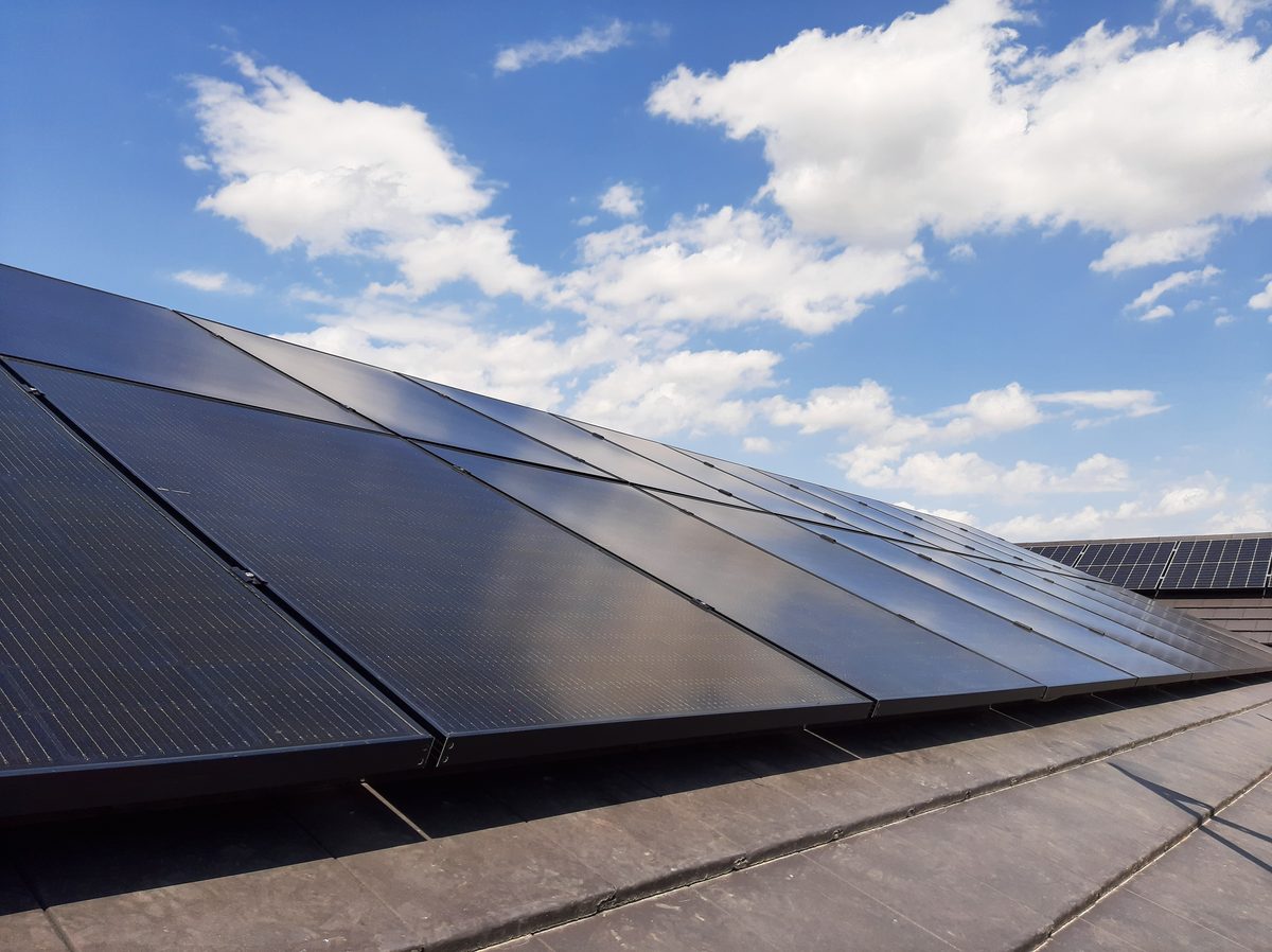 Schwarze Photovoltaik-Thermie-Module auf einem Schrägdach vor blauem Himmel