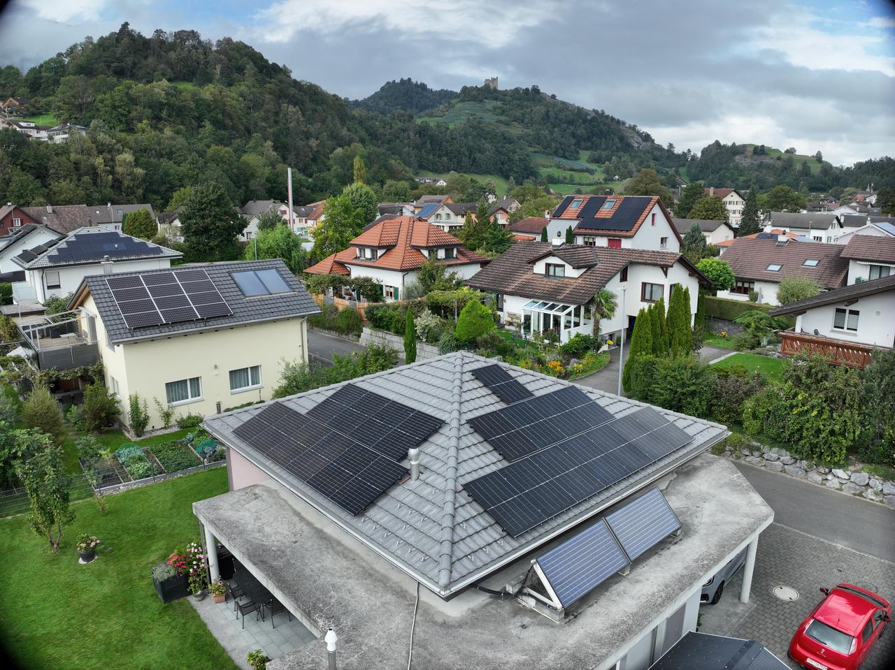 Luftaufnahme eines Einfamilienhauses mit Walmdach, schwarzen Photovoltaikmodulen und zusätzlichen Solarthermie-Kollektoren auf dem Vordach