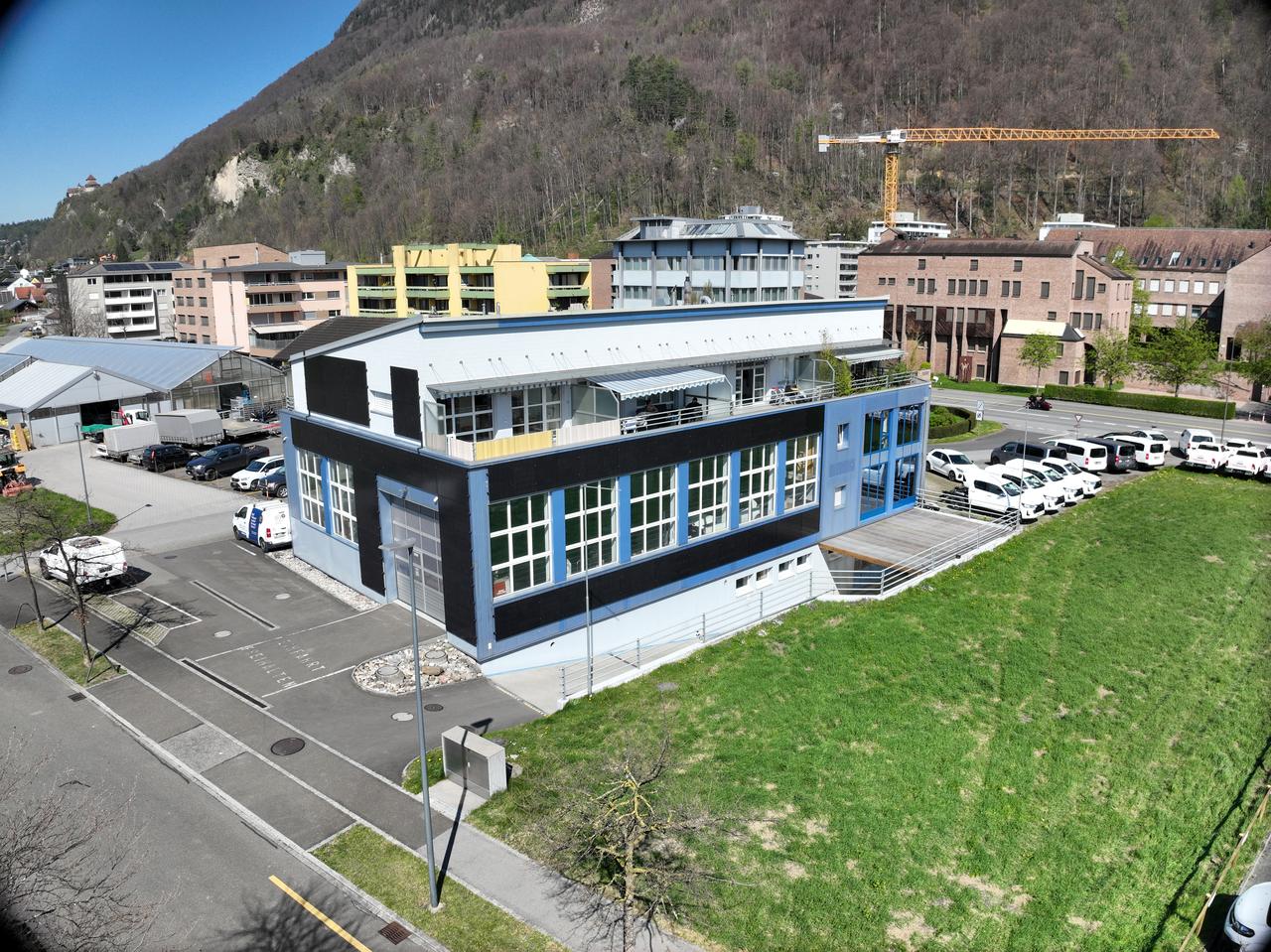 Luftaufnahme eines blau-weissen Gewerbegebäudes, dessen Fassade grossflächig mit schwarzen Photovoltaikmodulen verkleidet ist
