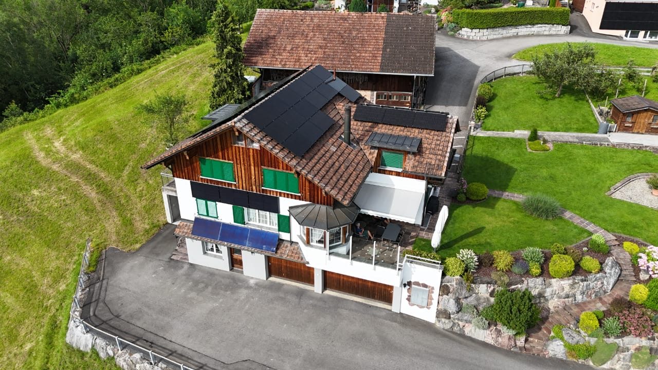 Luftaufnahme eines Chalets am Hang mit Photovoltaikmodulen auf dem Dach und zusätzlichen Modulen an der Fassade